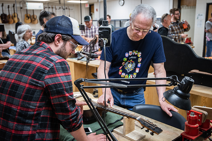 Men examining a guitar on a workbench.