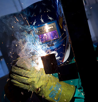 Welder with helmet working on metal beam