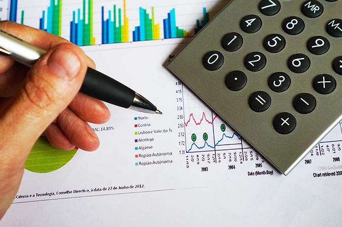 Hand holding a pen over paper charts with a calculator