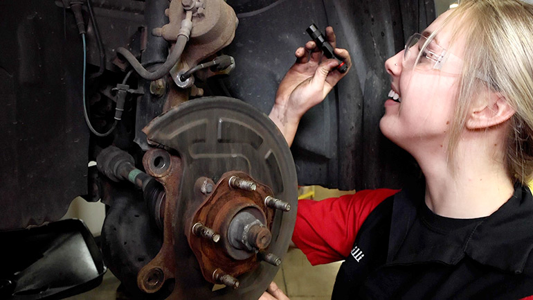 Mechanic in safety glasses examining a wheel well on a lifted car